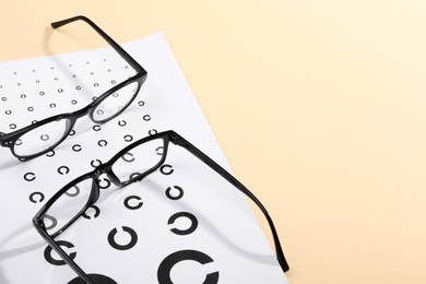 Photo of Vision test chart and glasses on beige background, space for text