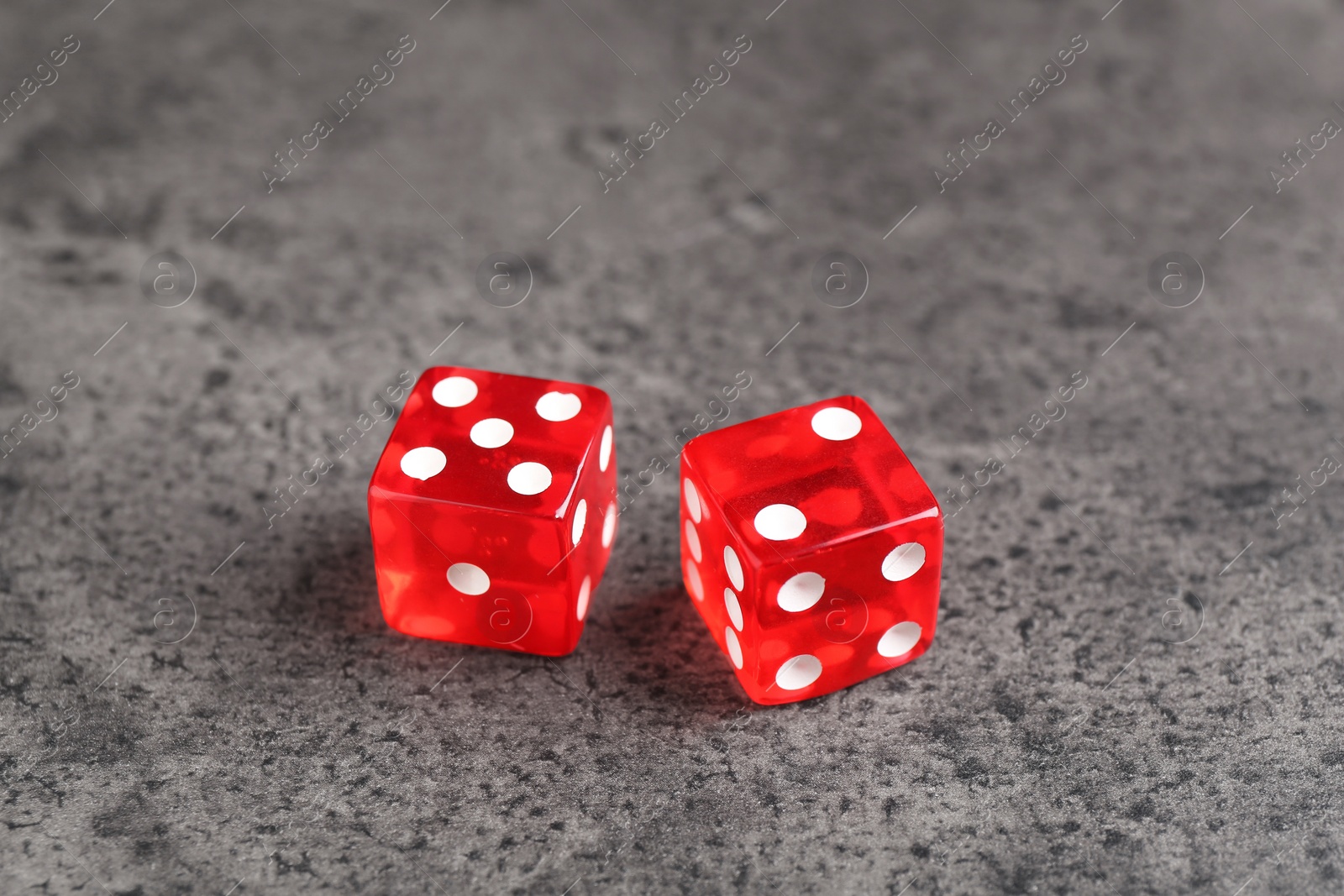 Photo of Two red game dices on grey textured table, closeup