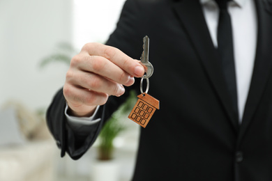 Real estate agent holding house key with trinket indoors, closeup