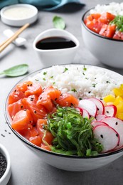 Delicious poke bowl with salmon and vegetables served on light grey table