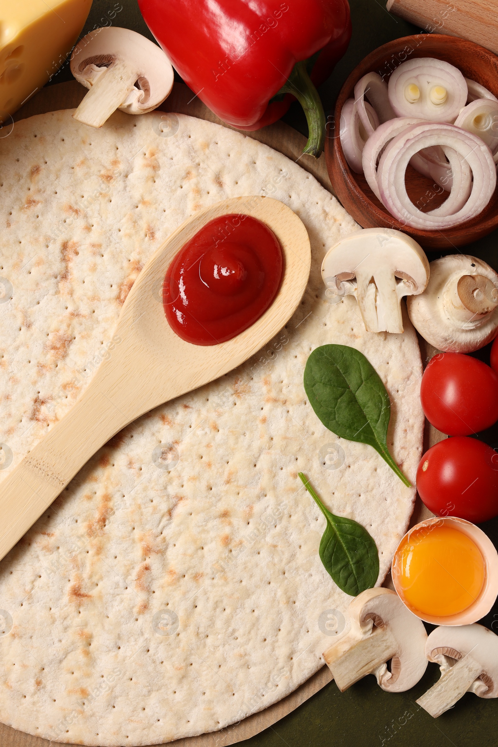 Photo of Pizza base, spoon with tomato sauce and products on dark table, flat lay