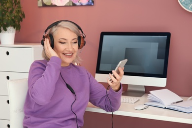 Photo of Mature woman listening to music on mobile phone at workplace