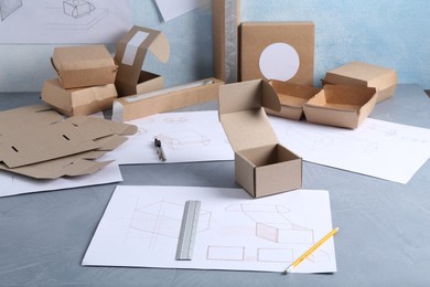 Photo of Creating packaging design. Drawings, boxes and stationery on blue textured table, closeup