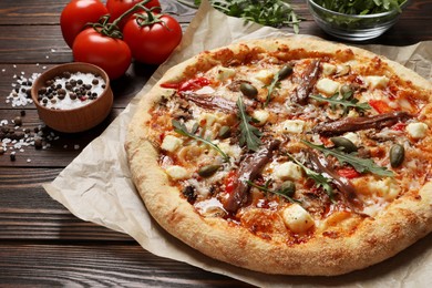 Photo of Tasty pizza with anchovies and ingredients on wooden table, closeup