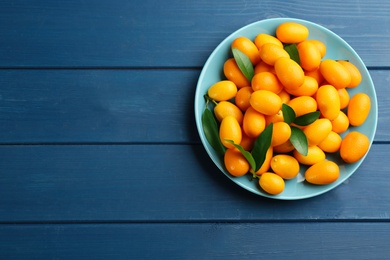 Photo of Fresh ripe kumquats on blue wooden table, top view. Space for text