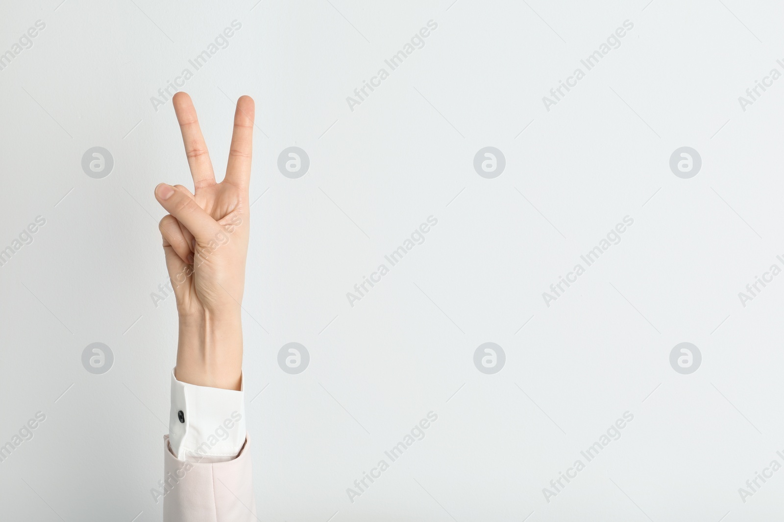 Photo of Young woman showing victory gesture on light background. Space for text