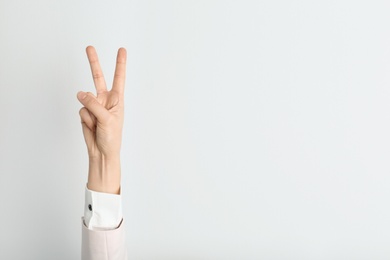 Photo of Young woman showing victory gesture on light background. Space for text