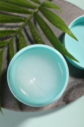 Lip balm and palm leaf on light blue background, top view