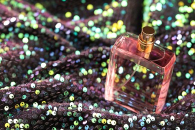 Photo of Luxury perfume in bottle on fabric with colorful sequins, closeup