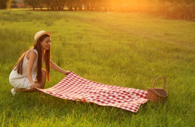 Photo of Young woman with picnic blanket and basket in park