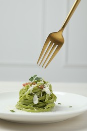 Photo of Eating tasty tagliatelle with spinach and cheese from plate at white wooden table, closeup. Exquisite presentation of pasta dish
