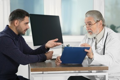 Photo of Senior doctor consulting patient at wooden table in clinic