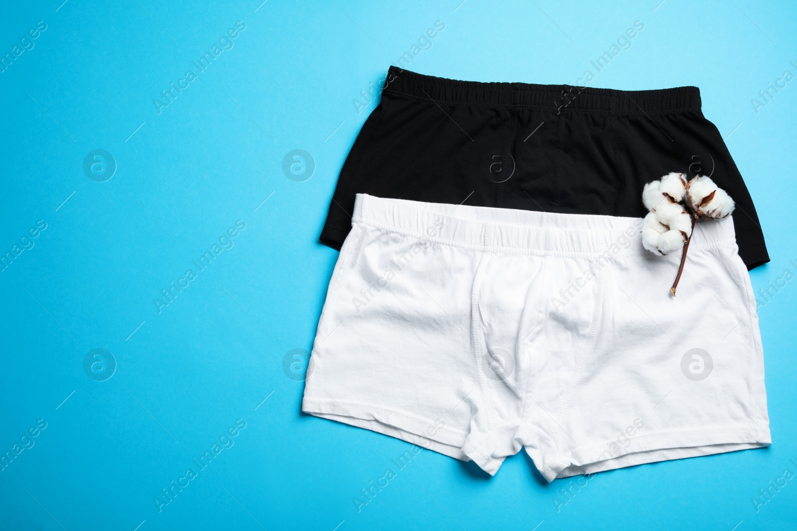 Photo of Comfortable men's underwear and cotton flowers on light blue background, flat lay. Space for text