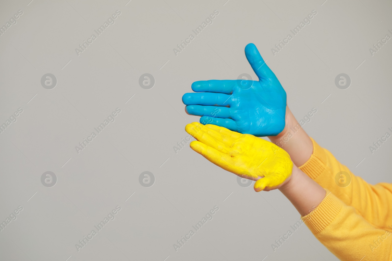 Photo of Little girl with hands painted in Ukrainian flag colors on light grey background, closeup and space for text. Love Ukraine concept