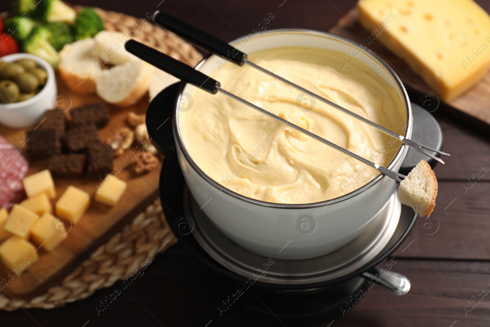 Photo of Fondue with tasty melted cheese, forks and different snacks on wooden table