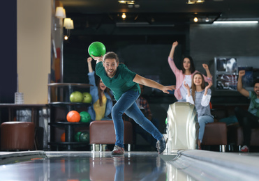 Photo of Young man throwing ball and spending time with friends in bowling club