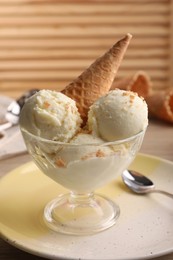 Photo of Delicious scoopsvanilla ice cream with wafer cone in glass dessert bowl on table, closeup