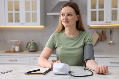 Woman measuring blood pressure with tonometer in kitchen