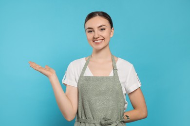 Beautiful young woman in clean apron with pattern on light blue background