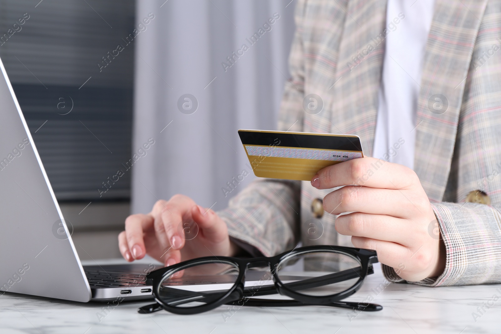 Photo of Online payment. Woman with laptop and credit card at white marble table, closeup