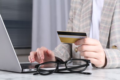 Online payment. Woman with laptop and credit card at white marble table, closeup