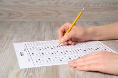 Student filling answer sheet at wooden table, closeup. Passing exam
