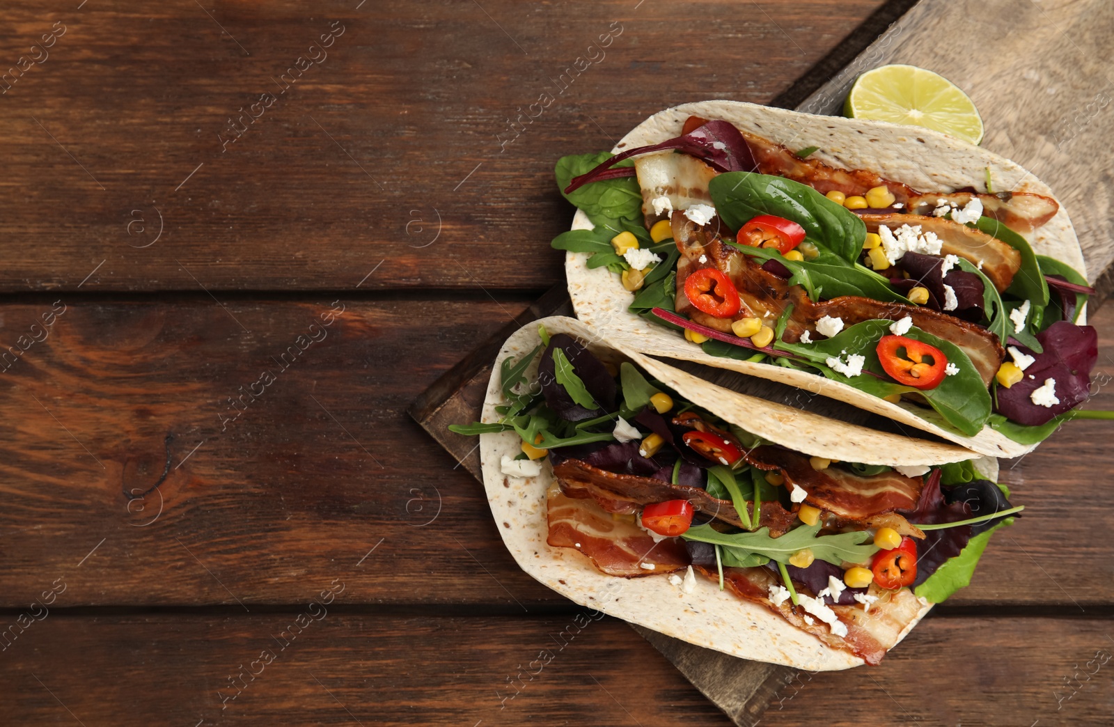 Photo of Delicious tacos with fried bacon, vegetables and cheese on wooden table, top view. Space for text