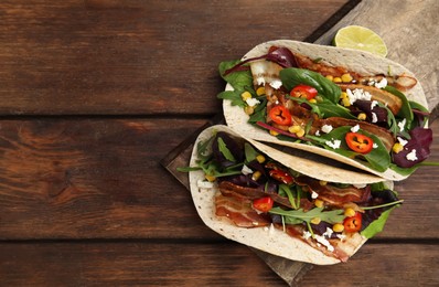 Photo of Delicious tacos with fried bacon, vegetables and cheese on wooden table, top view. Space for text