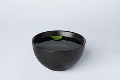 Water with green leaf in black bowl on white background
