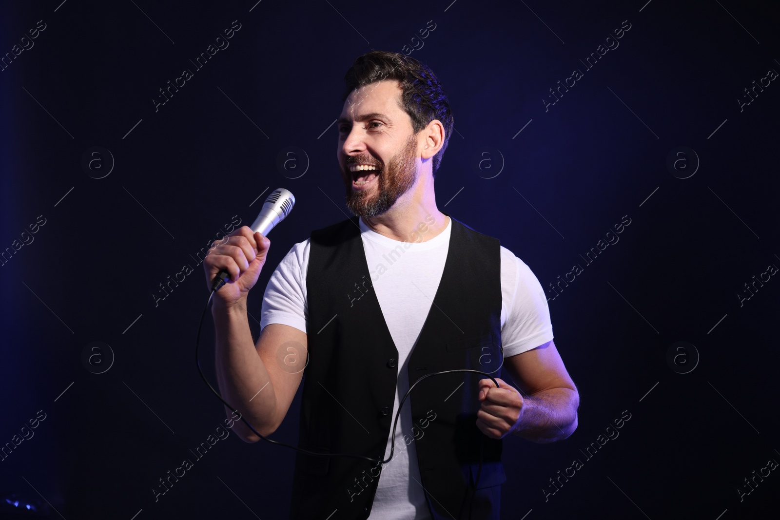 Photo of Handsome man with microphone singing on dark blue background