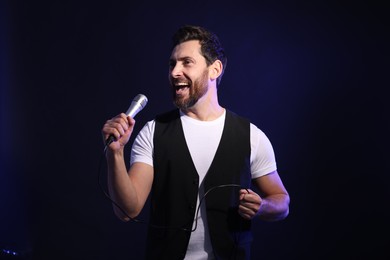 Photo of Handsome man with microphone singing on dark blue background