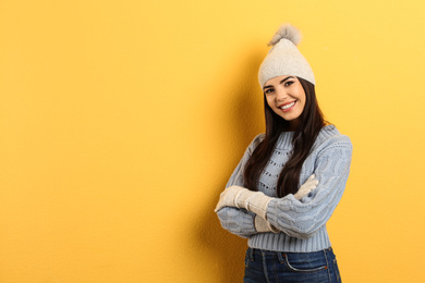 Happy young woman in warm clothes on yellow background, space for text. Winter vacation