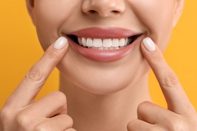 Woman showing her clean teeth and smiling on yellow background, closeup