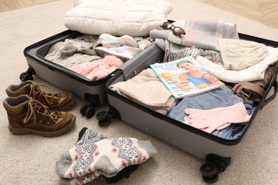Photo of Open suitcase with warm clothes, accessories and shoes on floor