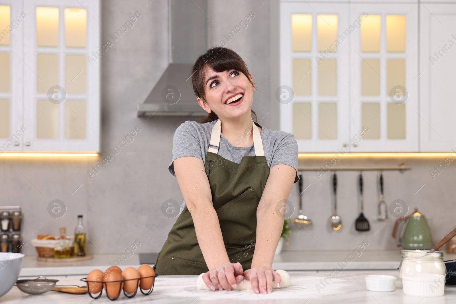 Photo of Happy young housewife kneading dough at white table in kitchen