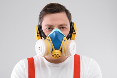 Photo of Male industrial worker in uniform on light background. Safety equipment