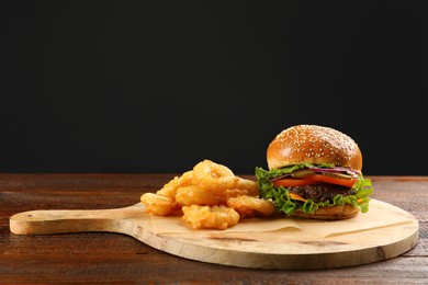 Photo of Burger and fried onion rings on wooden table, space for text. Fast food