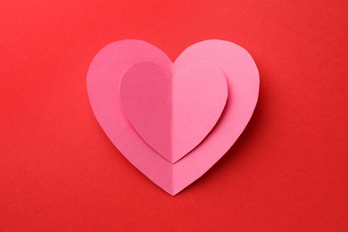 Pink paper hearts on red background, top view