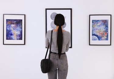 Photo of Young woman at exhibition in art gallery, back view