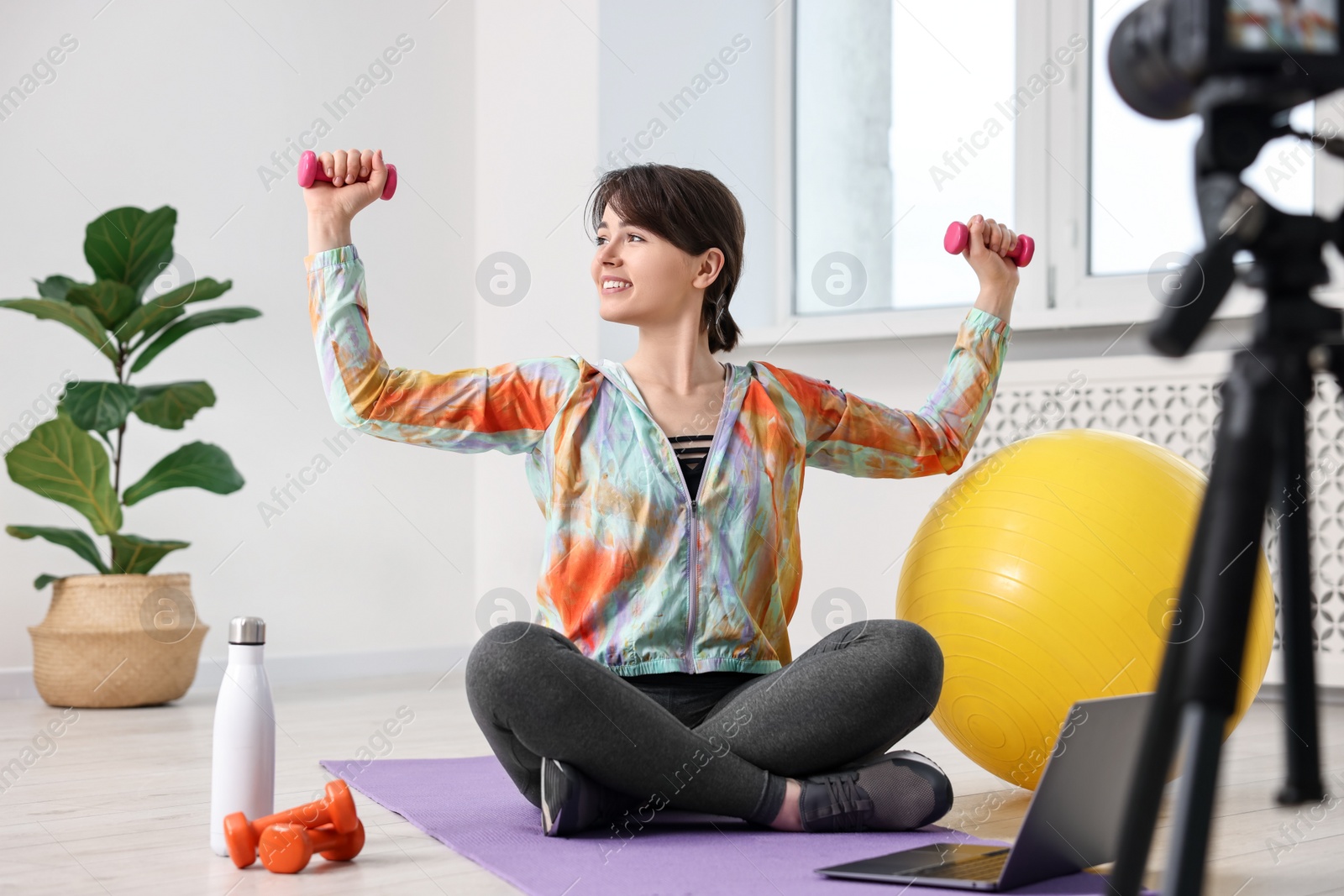 Photo of Happy sports blogger training with dumbbells while recording fitness lesson at home