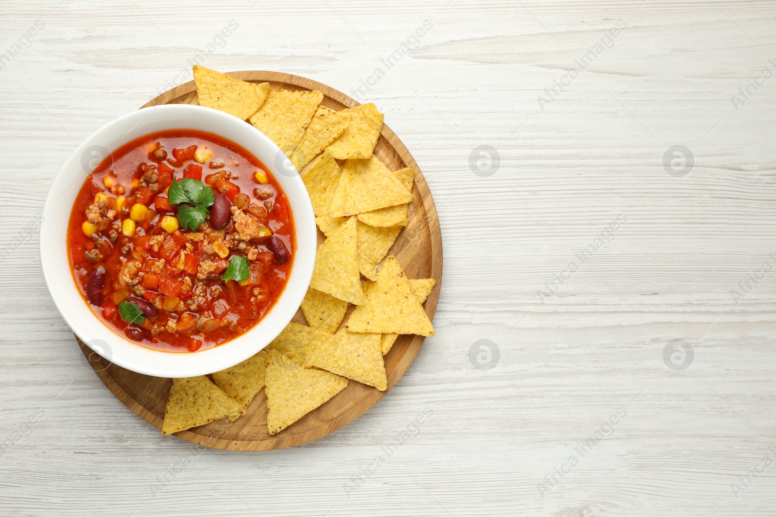 Photo of Bowl with tasty chili con carne and nachos on white wooden table, top view. Space for text