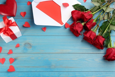 Photo of Flat lay composition with beautiful red roses and gift box on light blue background, space for text. Valentine's Day celebration