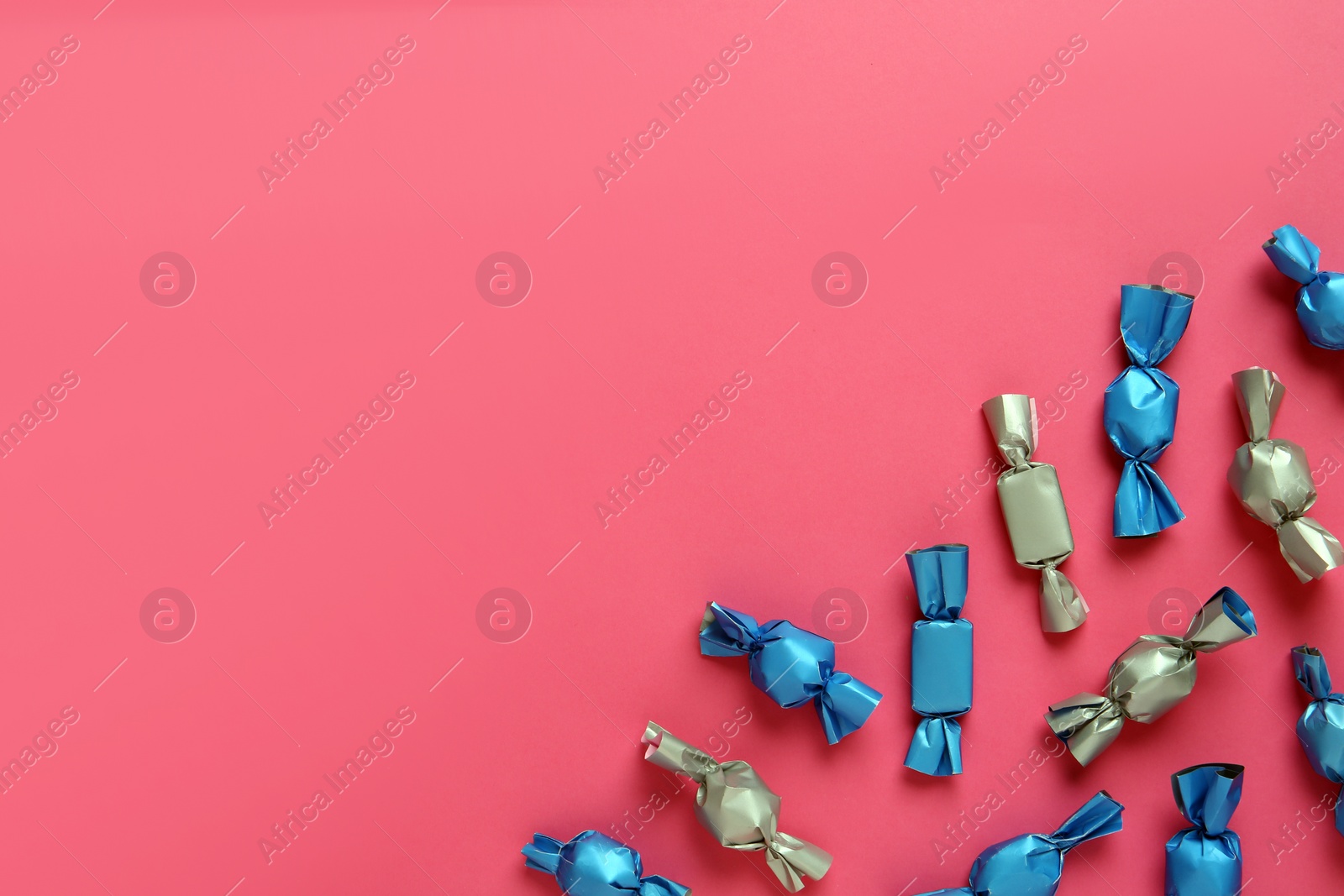 Photo of Candies in colorful wrappers on pink background, flat lay. Space for text