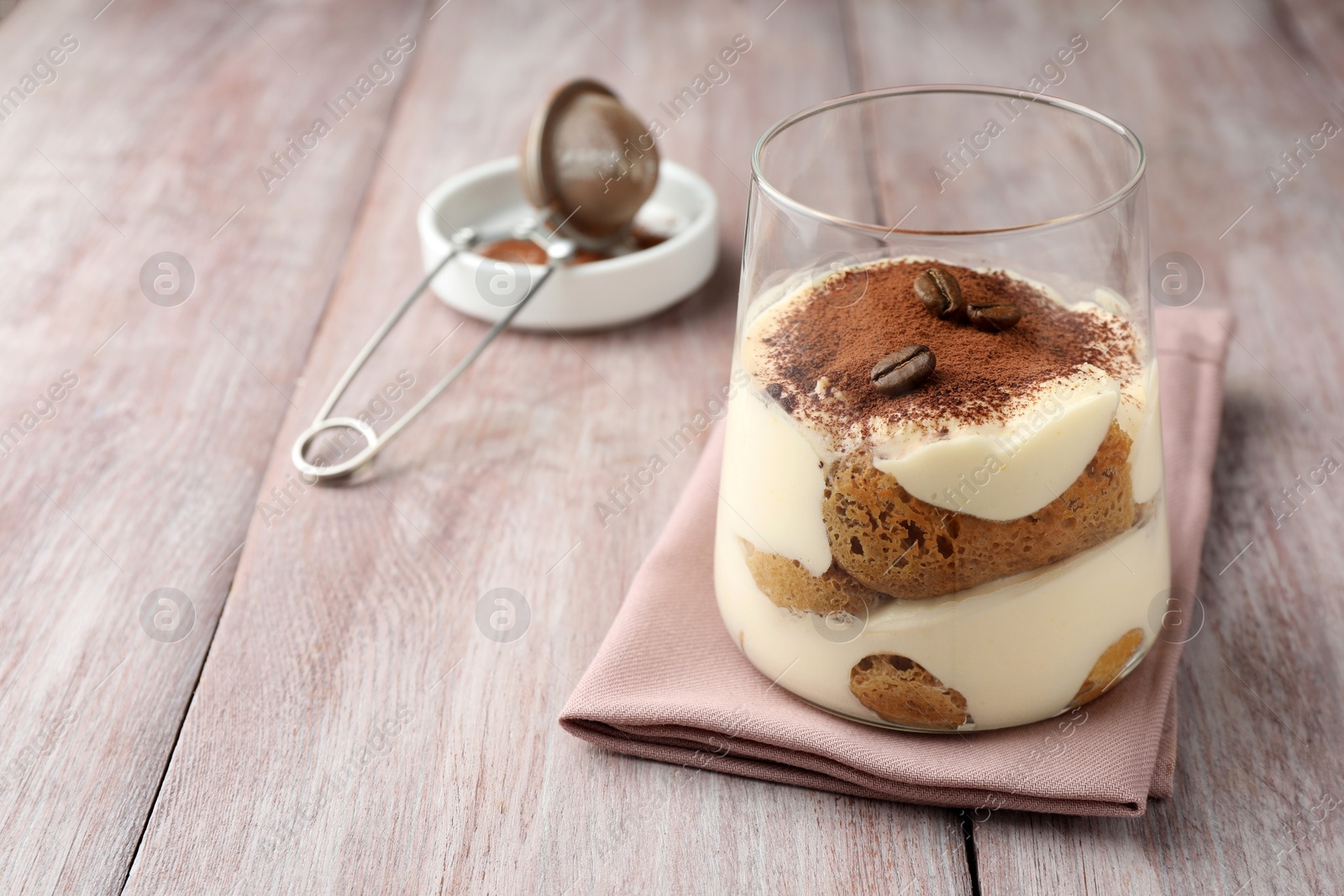 Photo of Delicious tiramisu with coffee beans in glass on wooden table, space for text