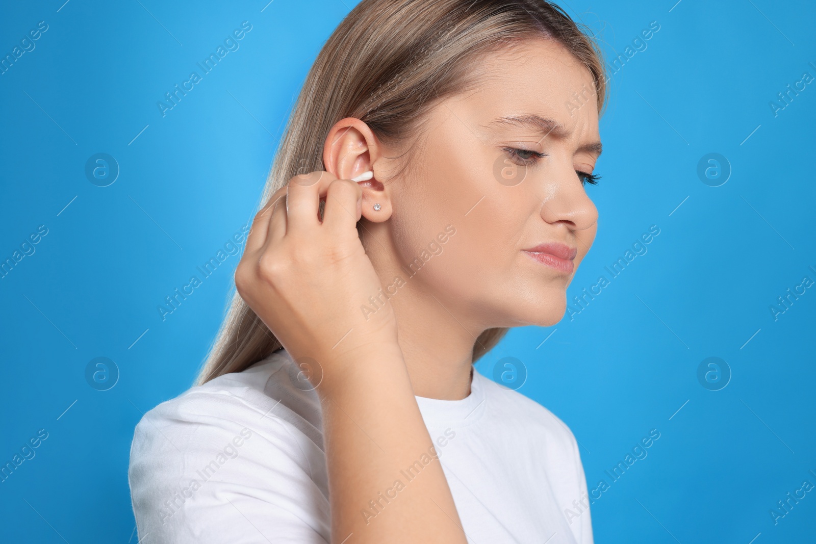 Photo of Young woman cleaning ear with cotton swab on light blue background