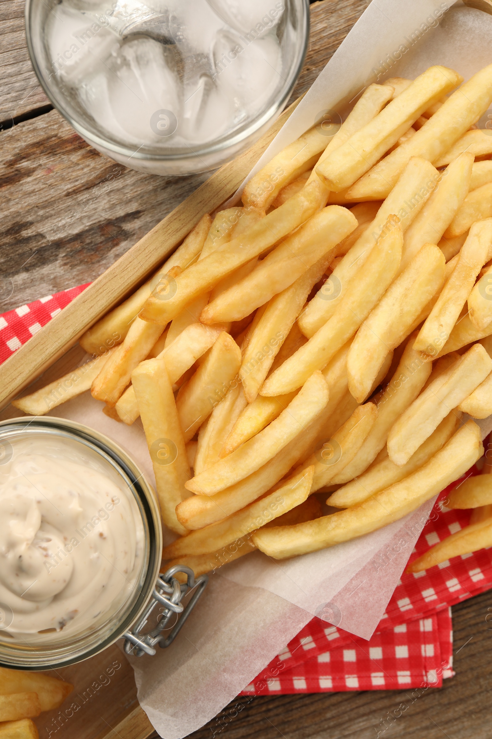 Photo of Delicious french fries served with sauce and glass of water on wooden table, flat lay