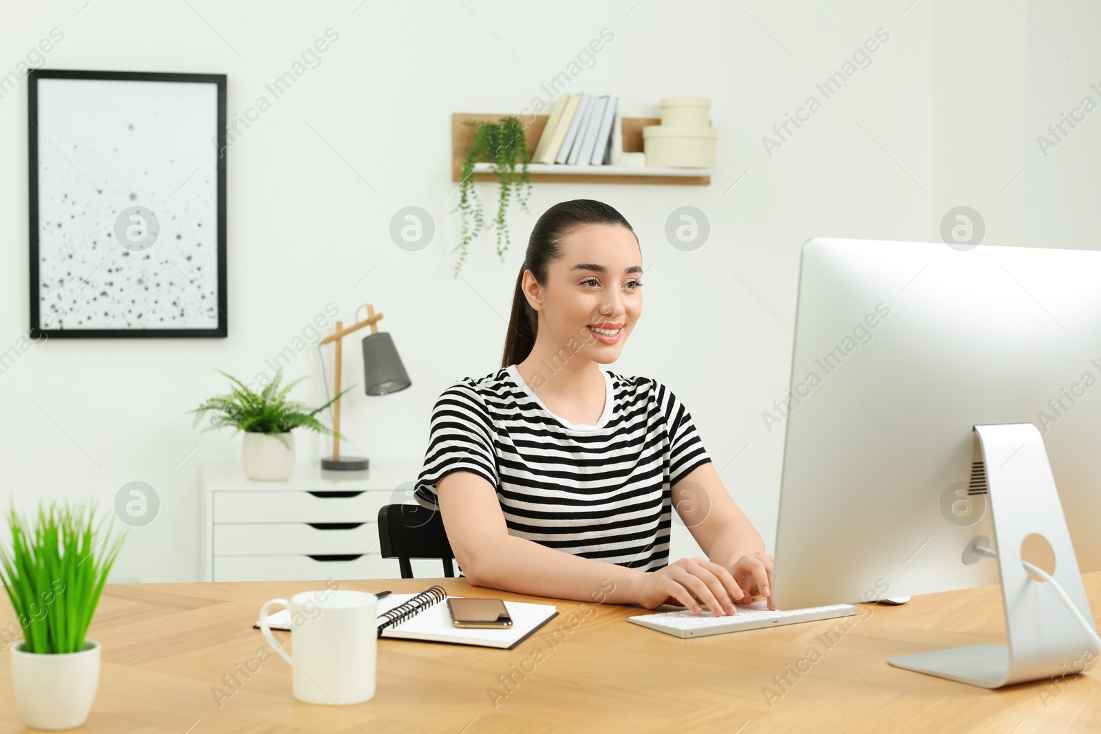 Photo of Home workplace. Happy woman working on computer at wooden desk in room