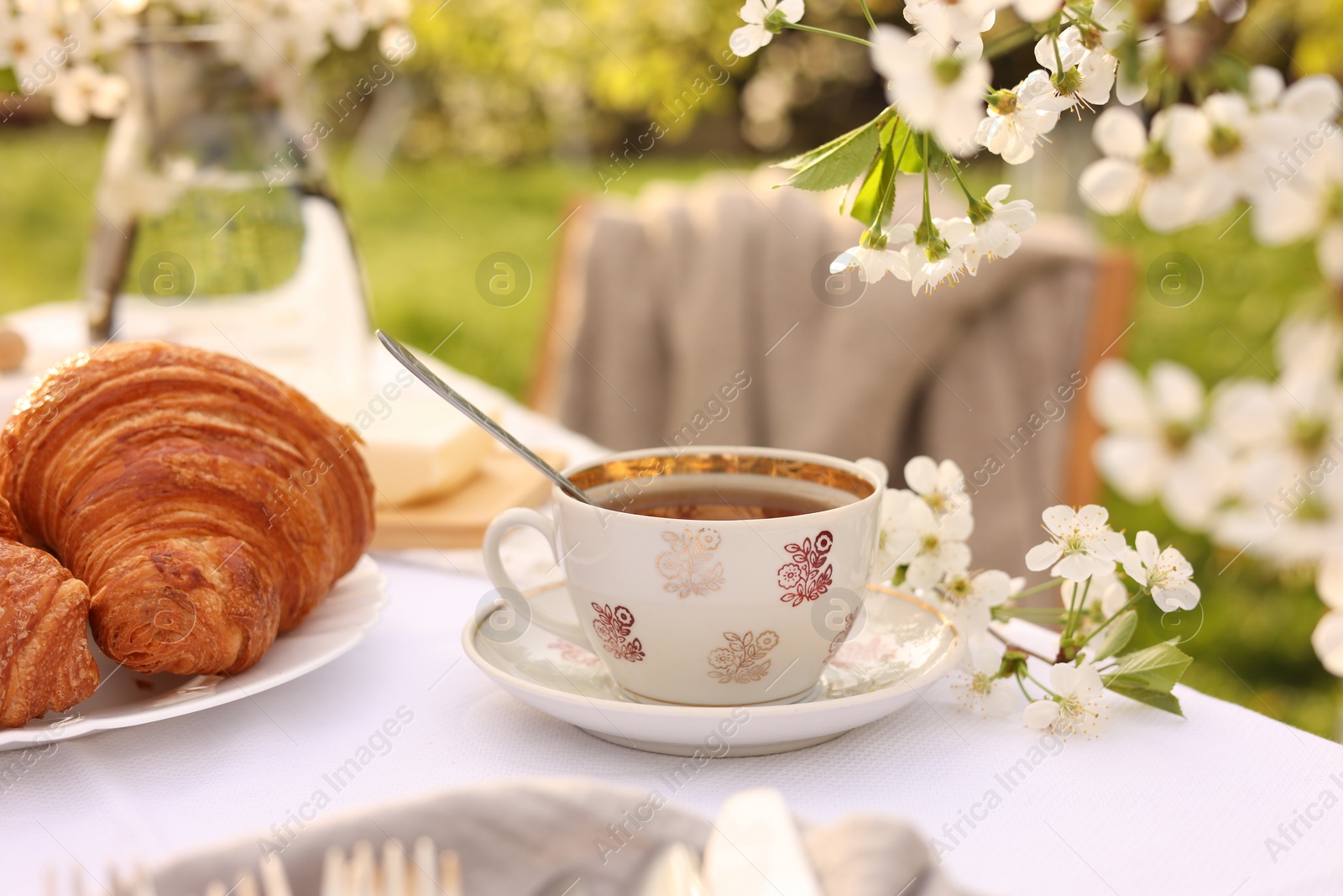 Photo of Stylish table setting with beautiful spring flowers, tea and croissants in garden