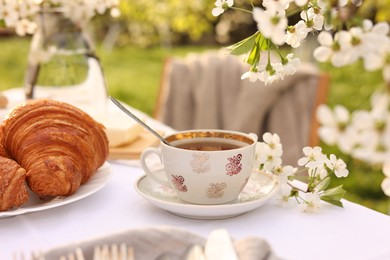 Stylish table setting with beautiful spring flowers, tea and croissants in garden