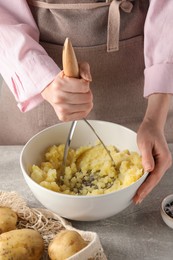 Woman making mashed potato at light grey table, closeup